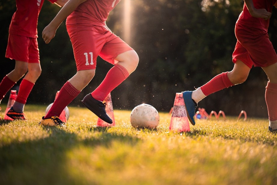 Children in red uniforms running soccer drills around cones